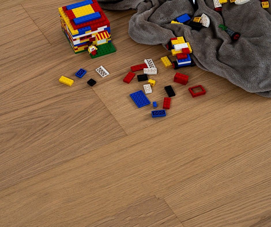 Lego sparsi su un pavimento di legno marrone chiaro, con una pila di pezzi crollati e un panno.