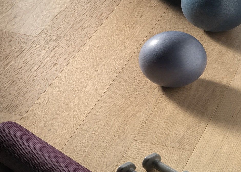Tappetino da yoga viola, palline grigie e manubri su un pavimento in legno chiaro.
