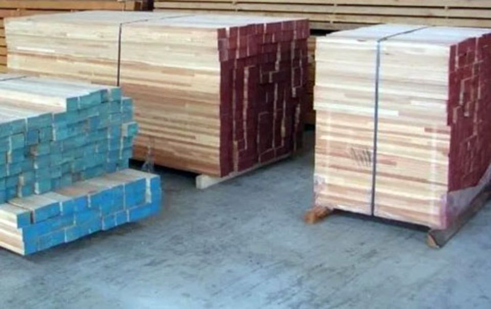 Fasci di legname, alcuni dipinti di blu o di rosso, accatastati su pallet in un magazzino.