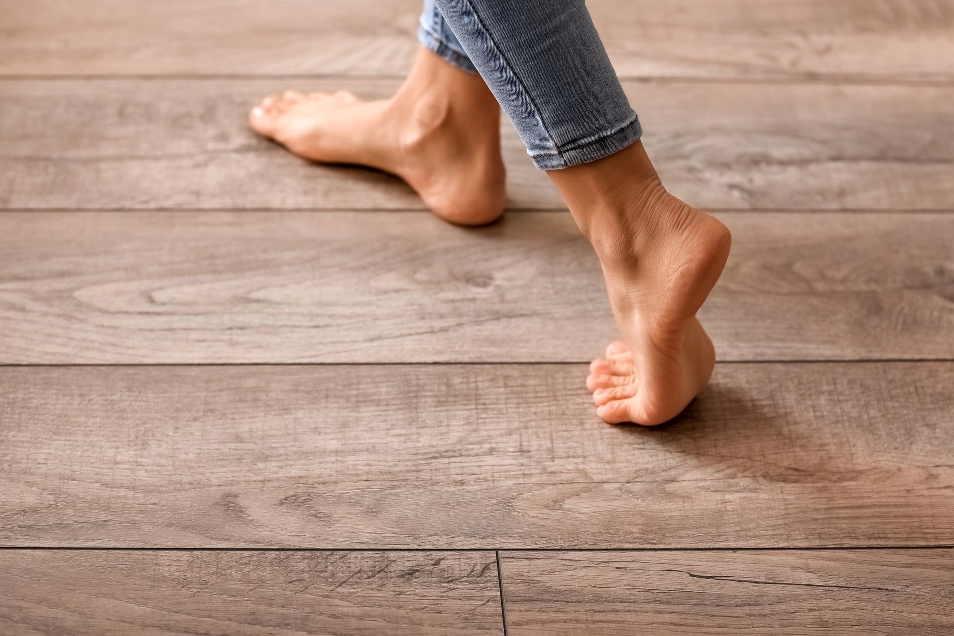 Piedi nudi che camminano su un pavimento in legno, indossando jeans.