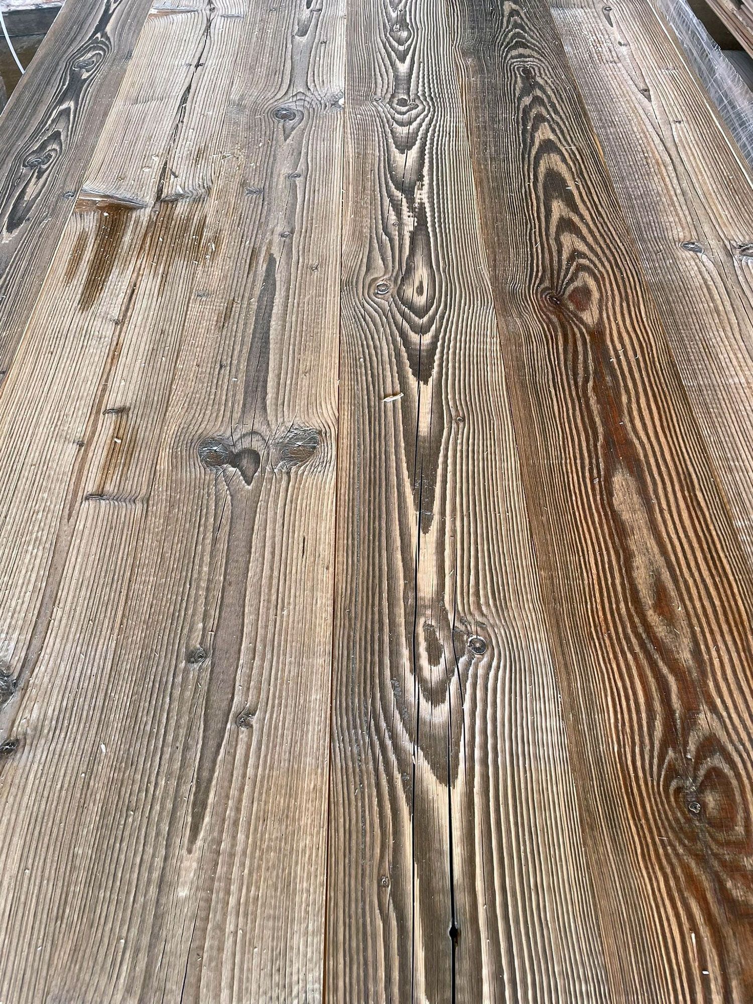 Primo piano di assi di legno stagionate, grigie e marroni, che mostrano le venature e i nodi del legno.