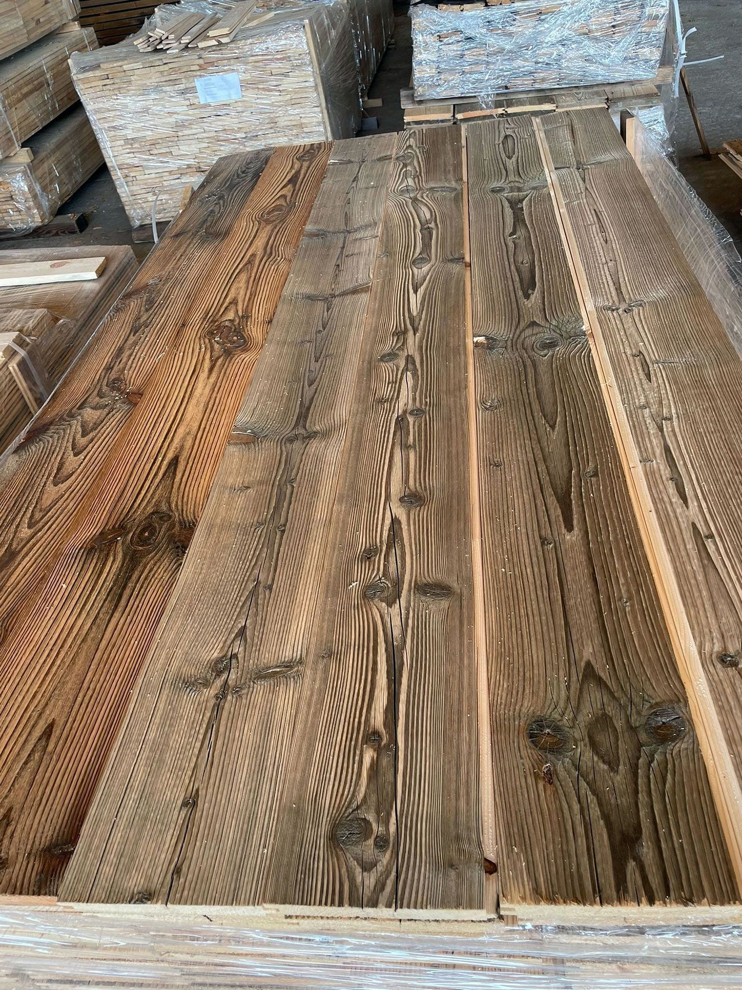 Assi di legno con nodi e un aspetto invecchiato e marrone, accatastate in un deposito di legname.