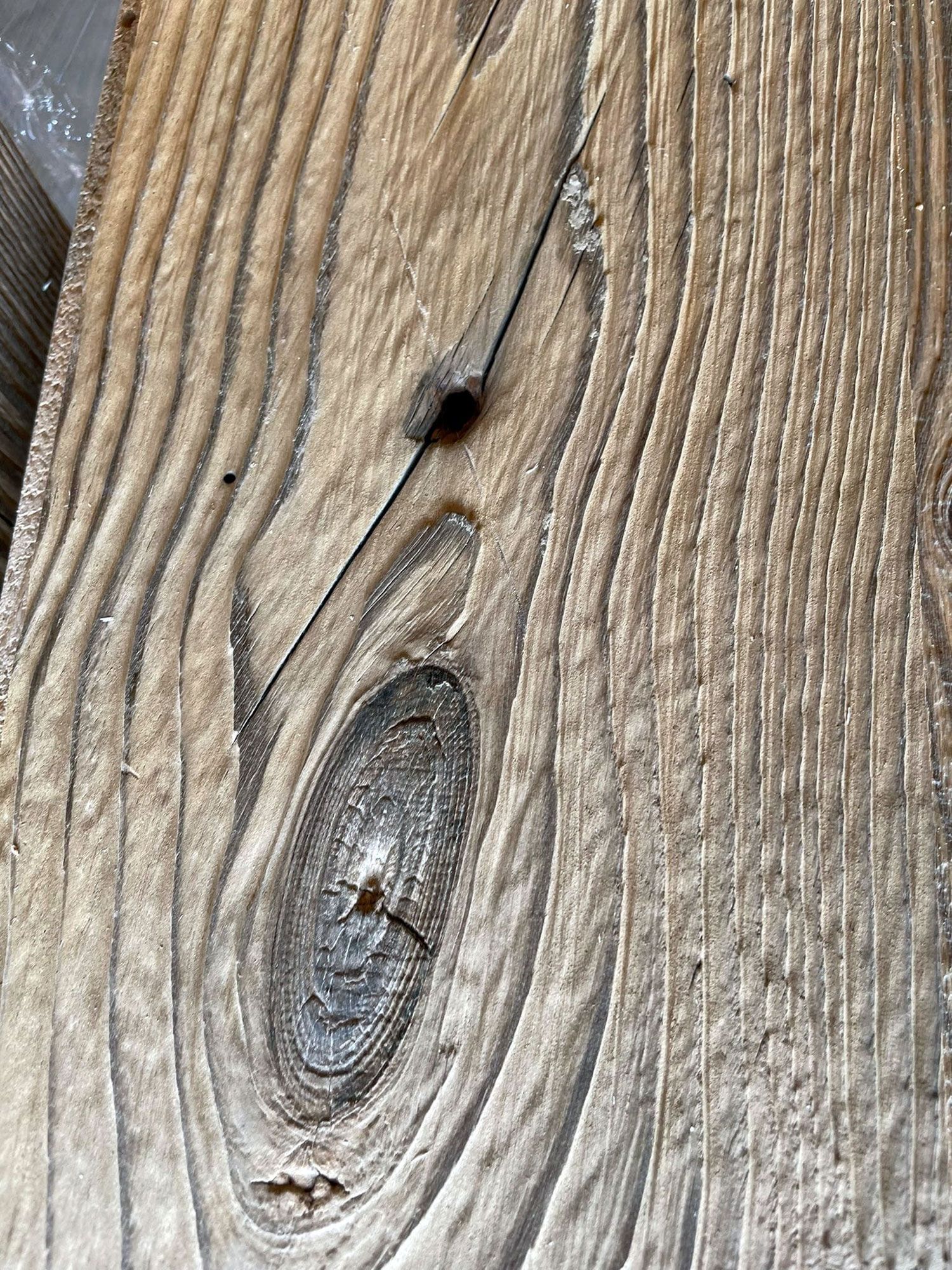 Primo piano di una tavola di legno stagionata, che mostra venature dettagliate e un nodo evidente.