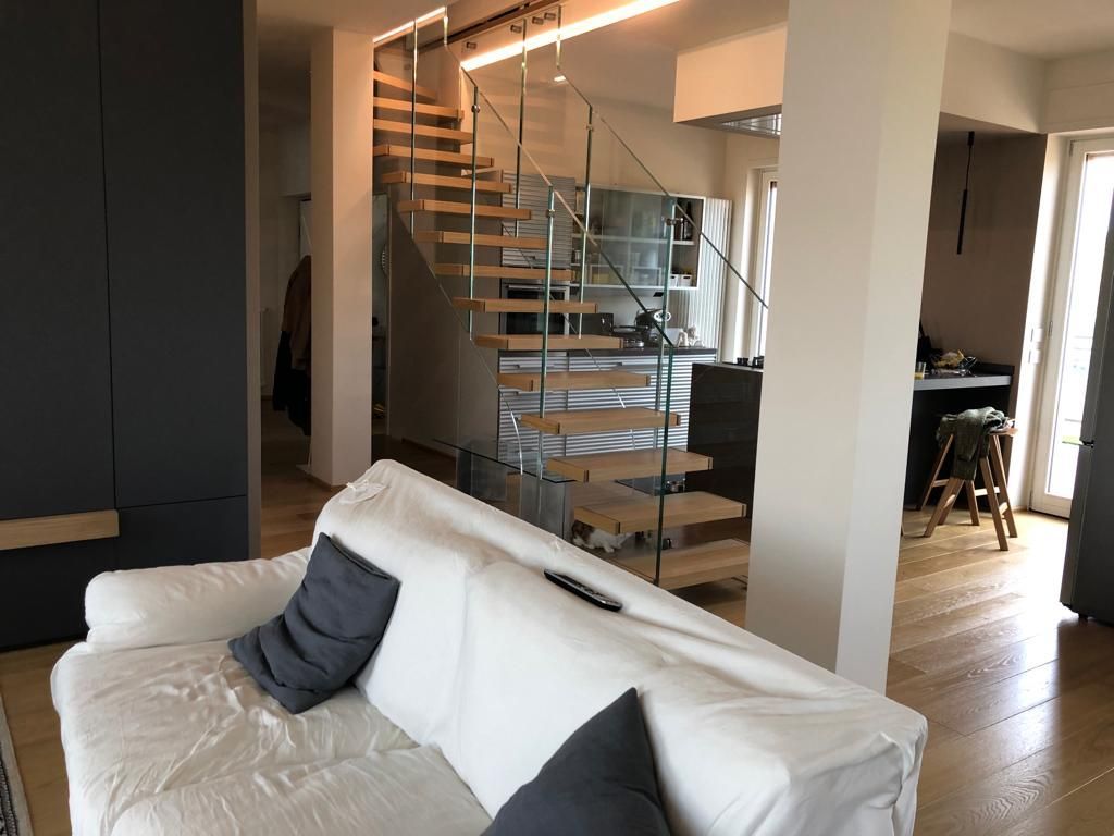 Soggiorno moderno con divano bianco, scala in legno e cucina a vista.