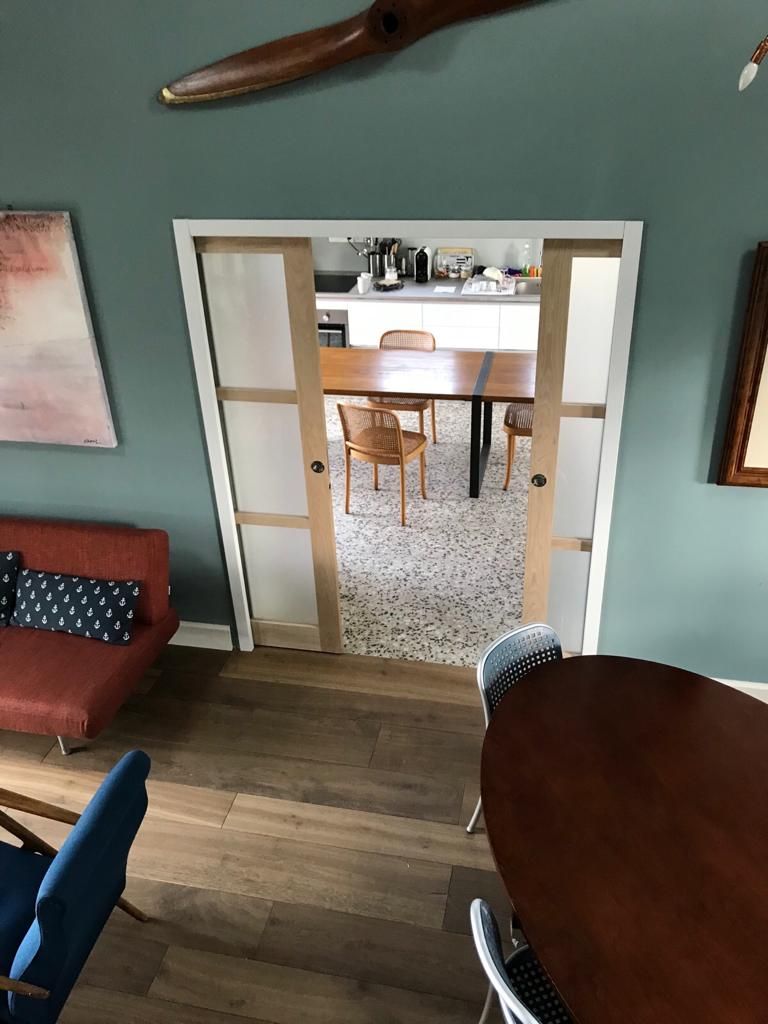 Vista dal soggiorno verso la cucina, attraverso una porta con porte scorrevoli aperte con cornice in legno chiaro.