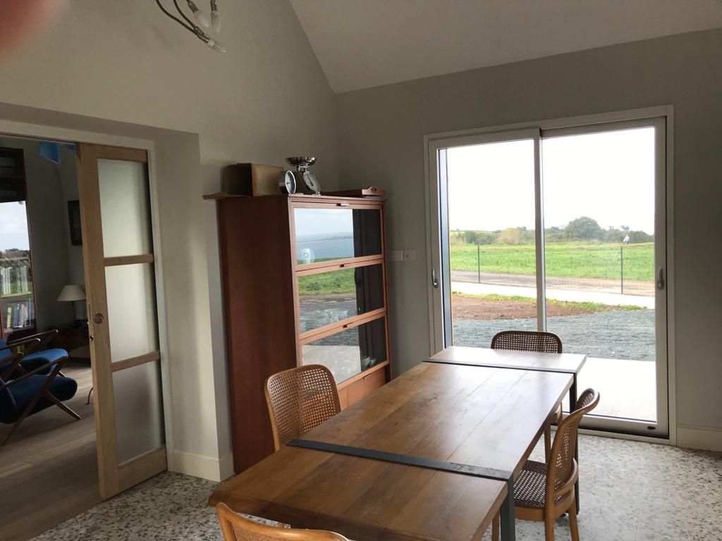 Zona pranzo con tavolo in legno, sedie e porta scorrevole in vetro con vista su un campo.