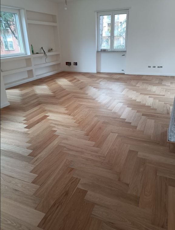 Pavimento in parquet di rovere chiaro in una stanza luminosa con scaffali incorporati e due finestre.