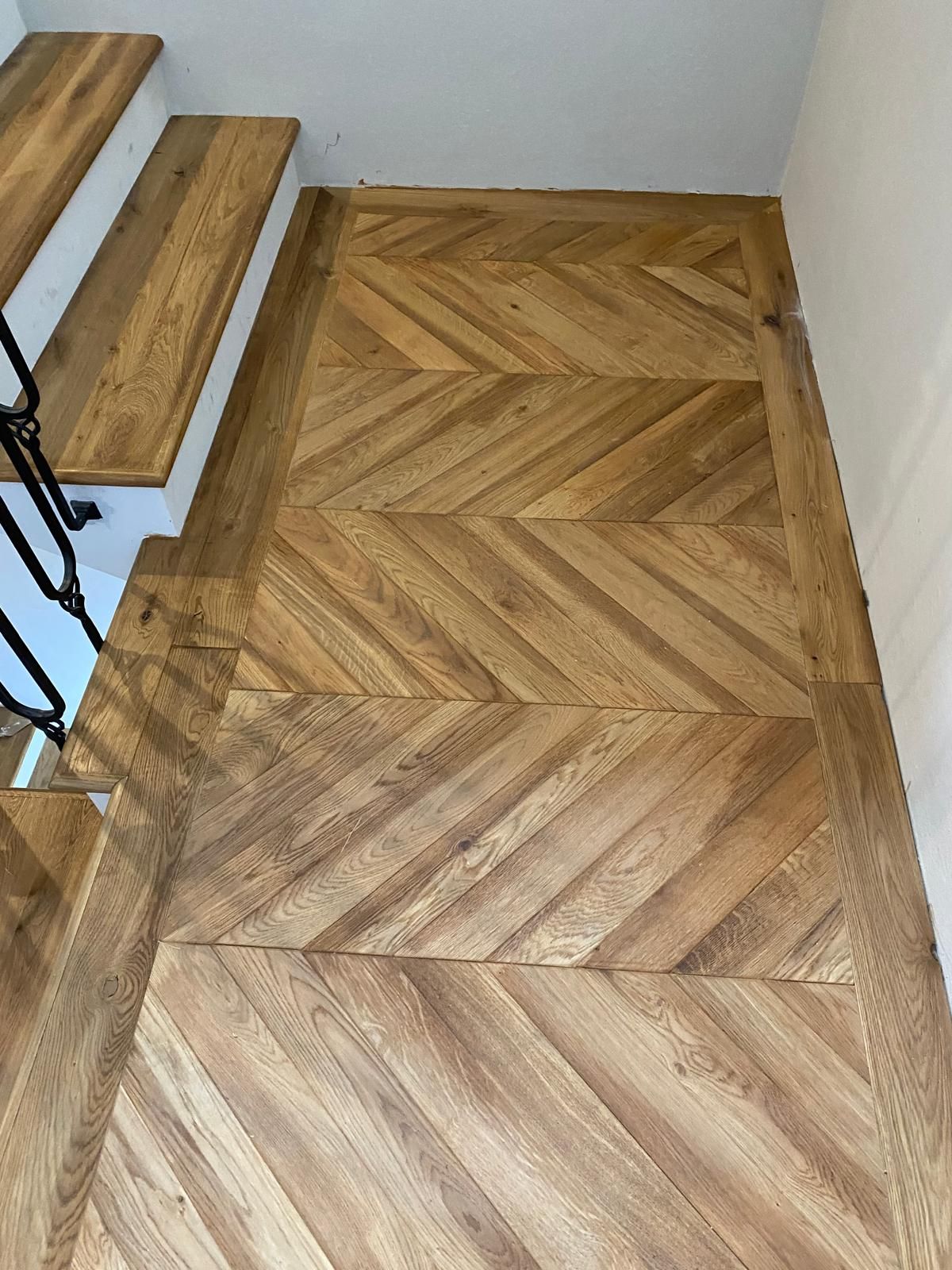 Pavimento e scale in legno a spina di pesce con pareti bianche e ringhiera nera.