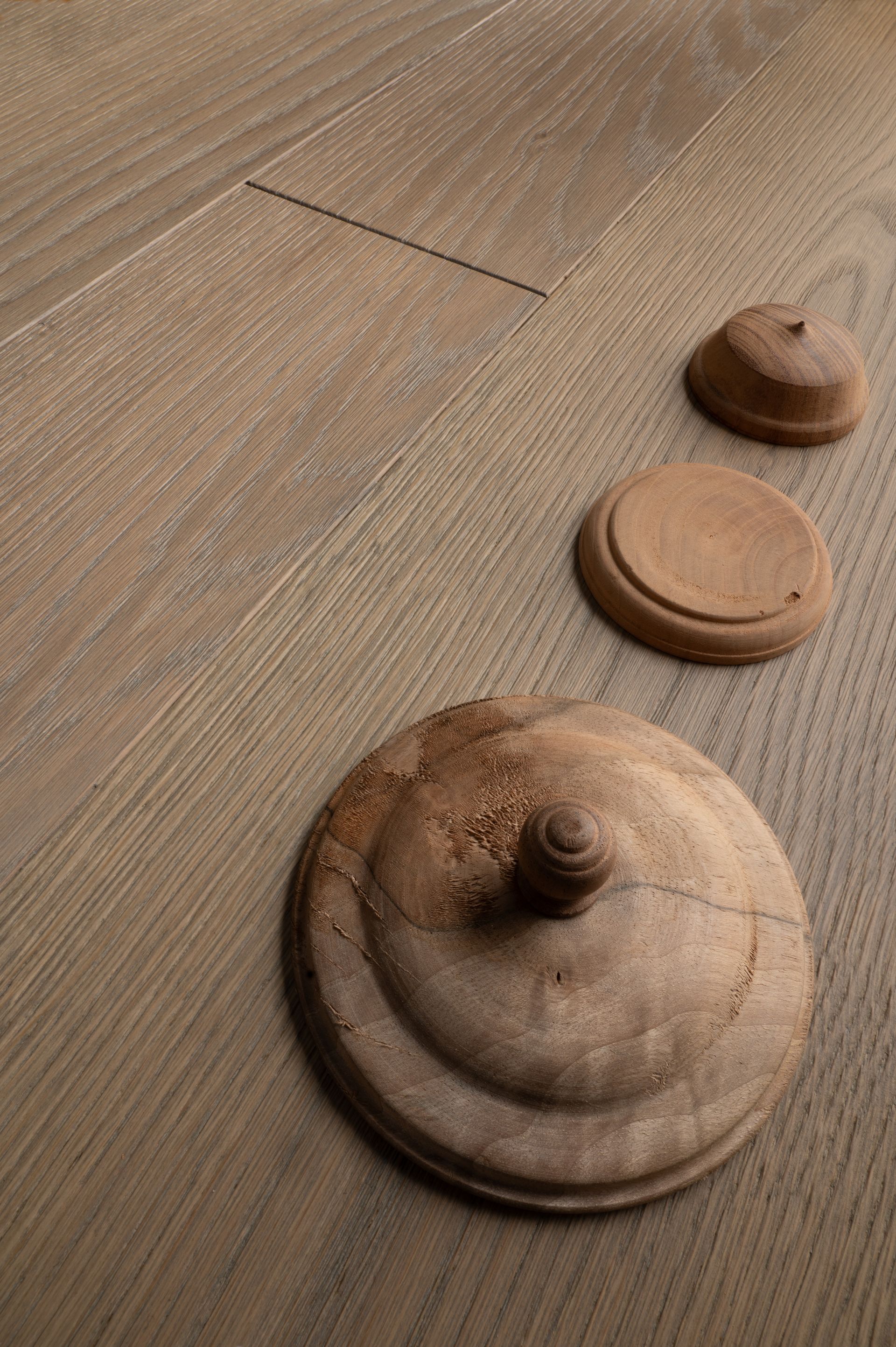 Tre pezzi decorativi in legno di varie dimensioni su un pavimento in legno marrone chiaro.