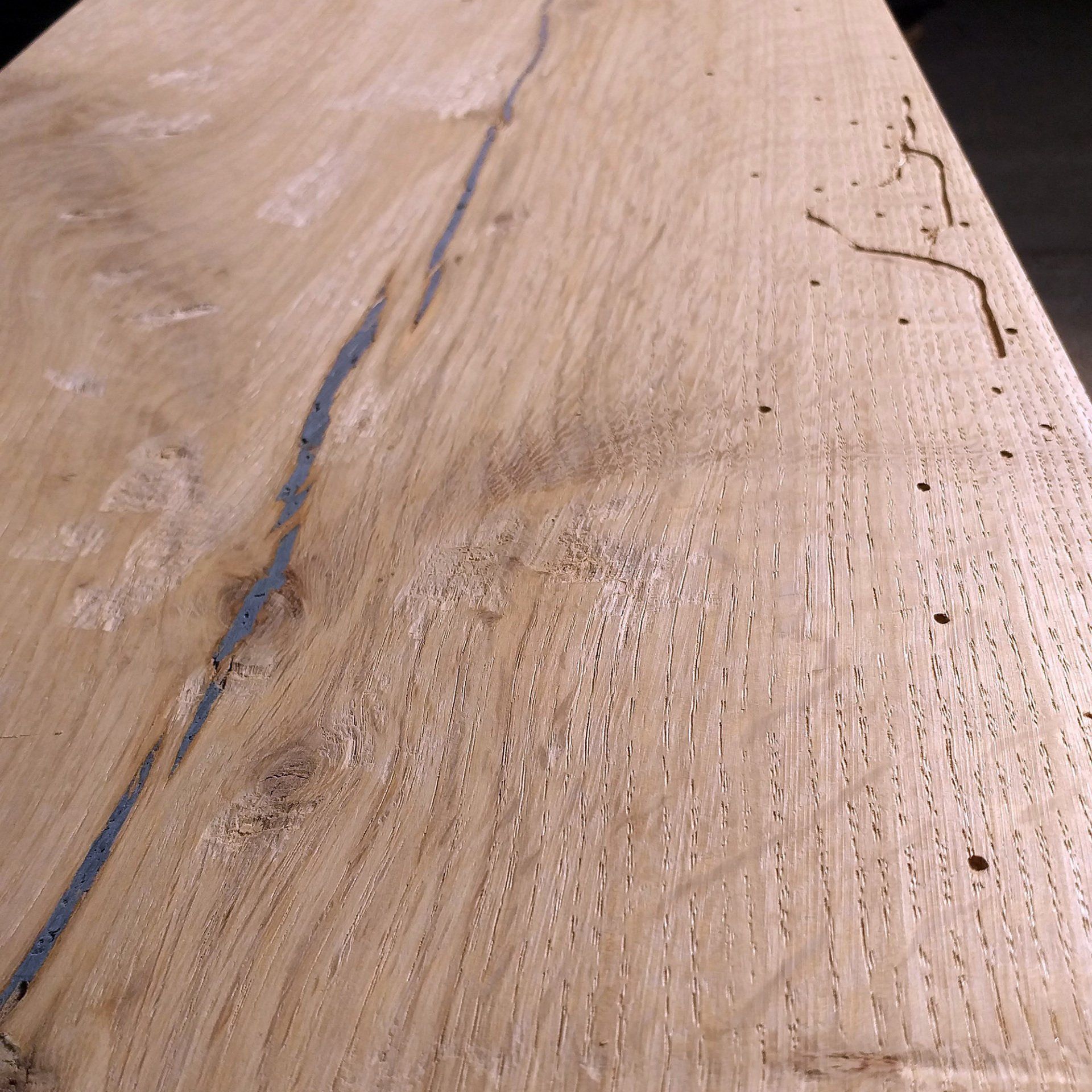 Primo piano di una tavola di legno chiara con venature, una crepa e fori di insetti.