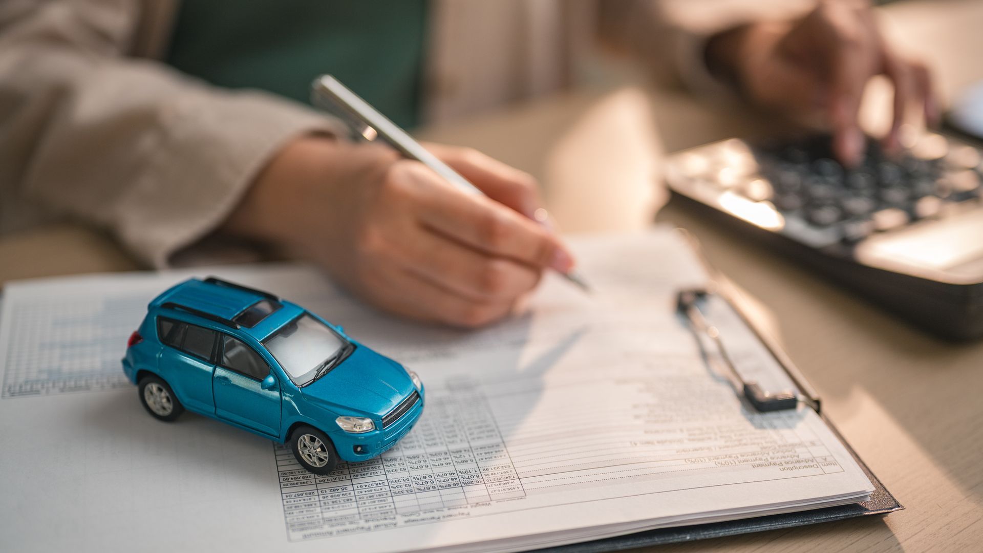 Toy car on insurance documents while a person completes paperwork and calculations.