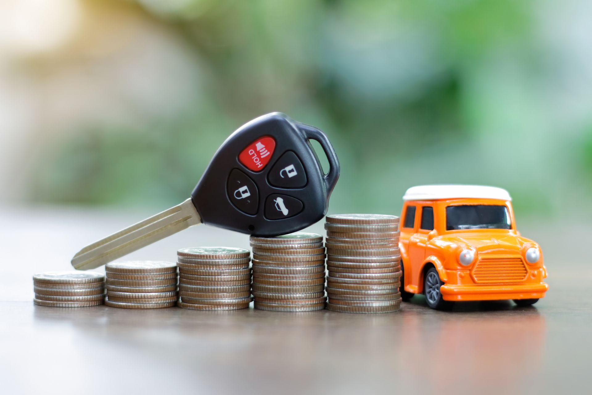 Car keys on a pile of coins and a model car.