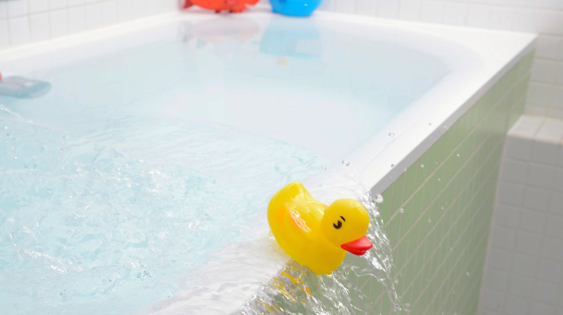 Yellow rubber duck floating at the edge of a white bathtub filled with water
