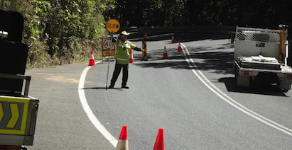 A Man Is Standing On The Side Of A Road Holding A Sign — PTS Traffic Management in Smithfield, QLD