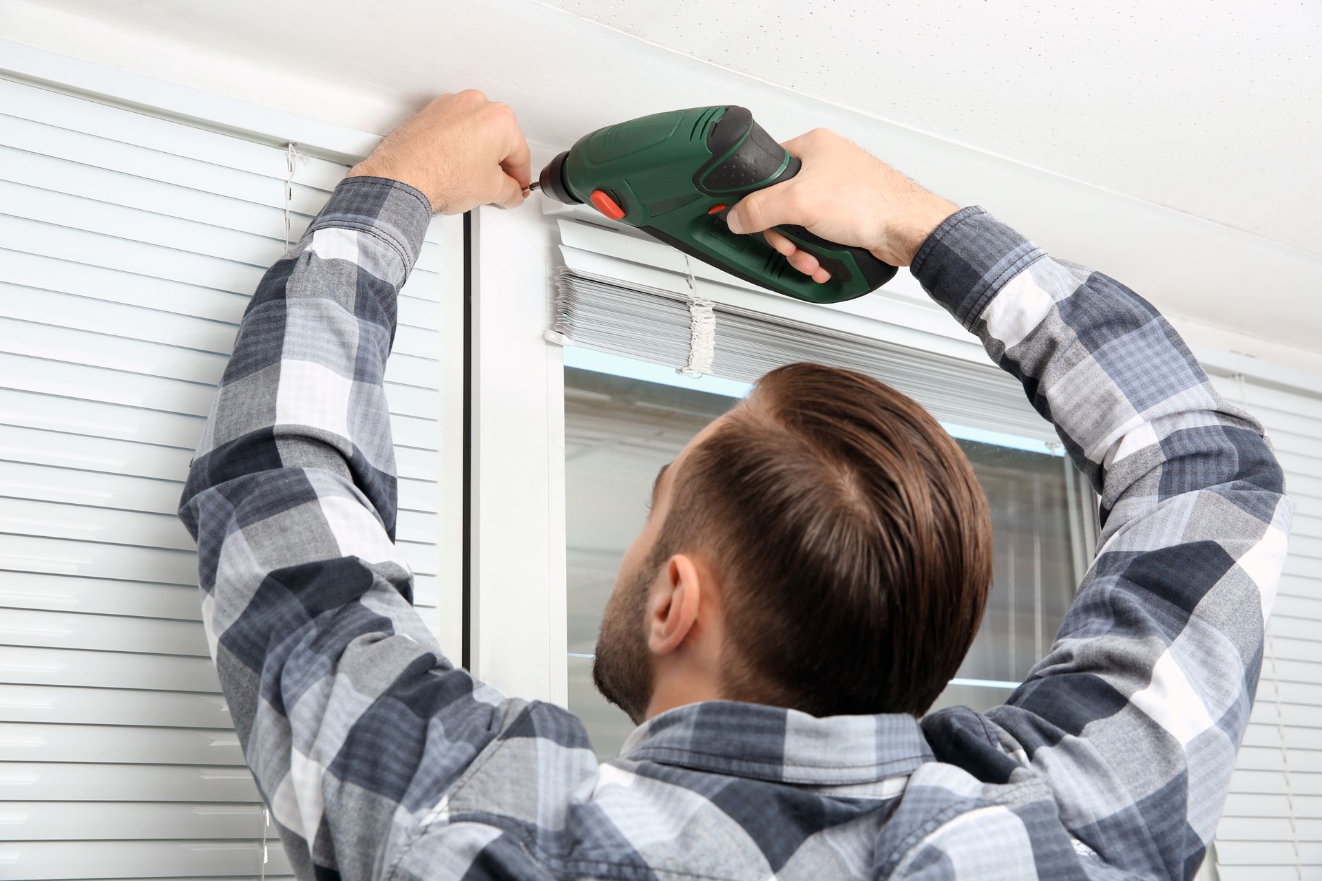 Person using a drill to install a window blind above a window