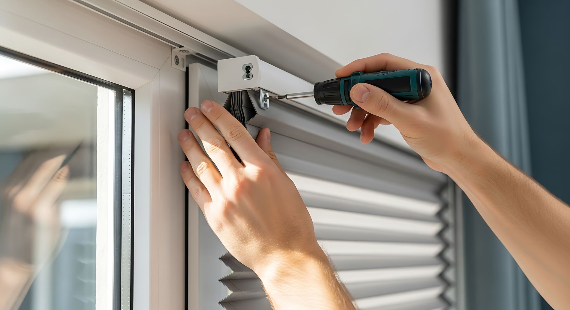 Hands installing a window blind bracket with a screwdriver beside a window