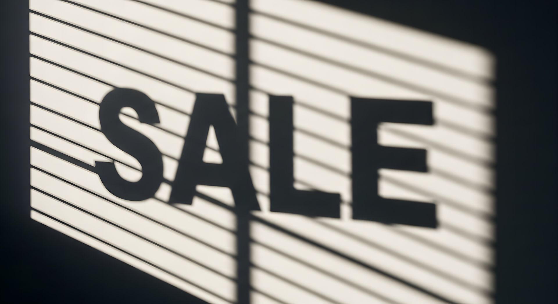 SALE sign in bold black letters on a white background with window blinds casting shadows