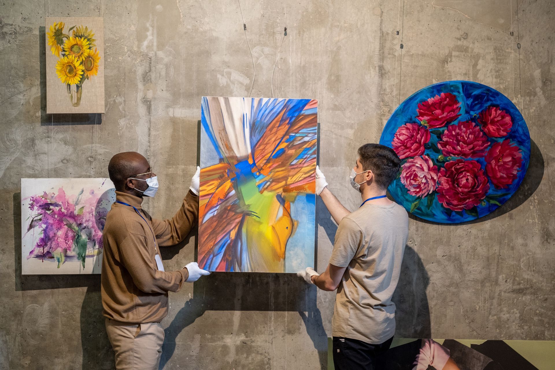 Two people discuss a colorful abstract painting displayed on a concrete gallery wall.