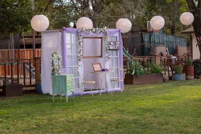 Lavender outdoor bookshelf display with hanging floral decorations and white lanterns on a grassy lawn.