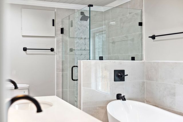 Bright modern bathroom with glass shower enclosure, white tiles, and double sinks