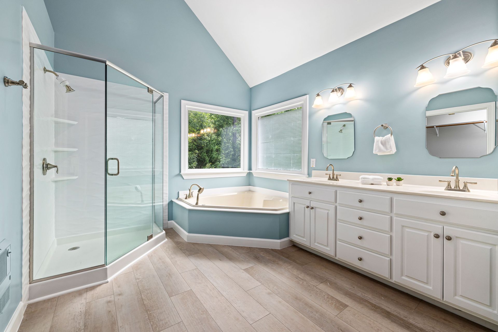 Bright bathroom with a glass shower, corner tub, double vanity, and light blue walls