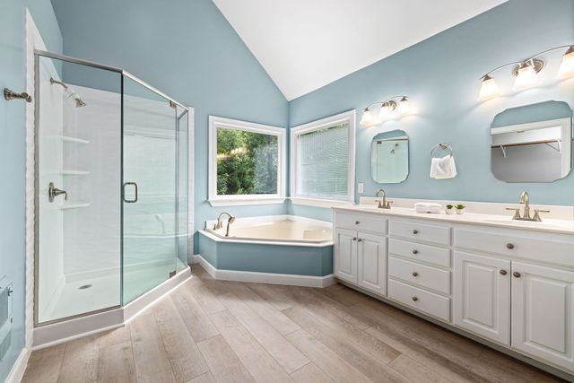 Bright bathroom with a glass shower, corner tub, double vanity, and light blue walls