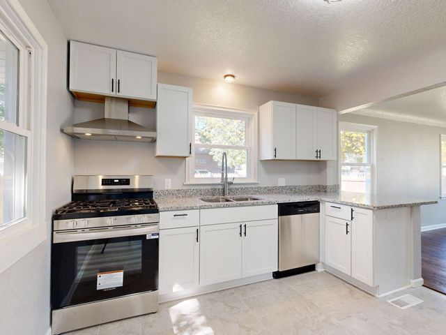 Bright kitchen with white cabinets, black stove, and granite countertops beside a window.