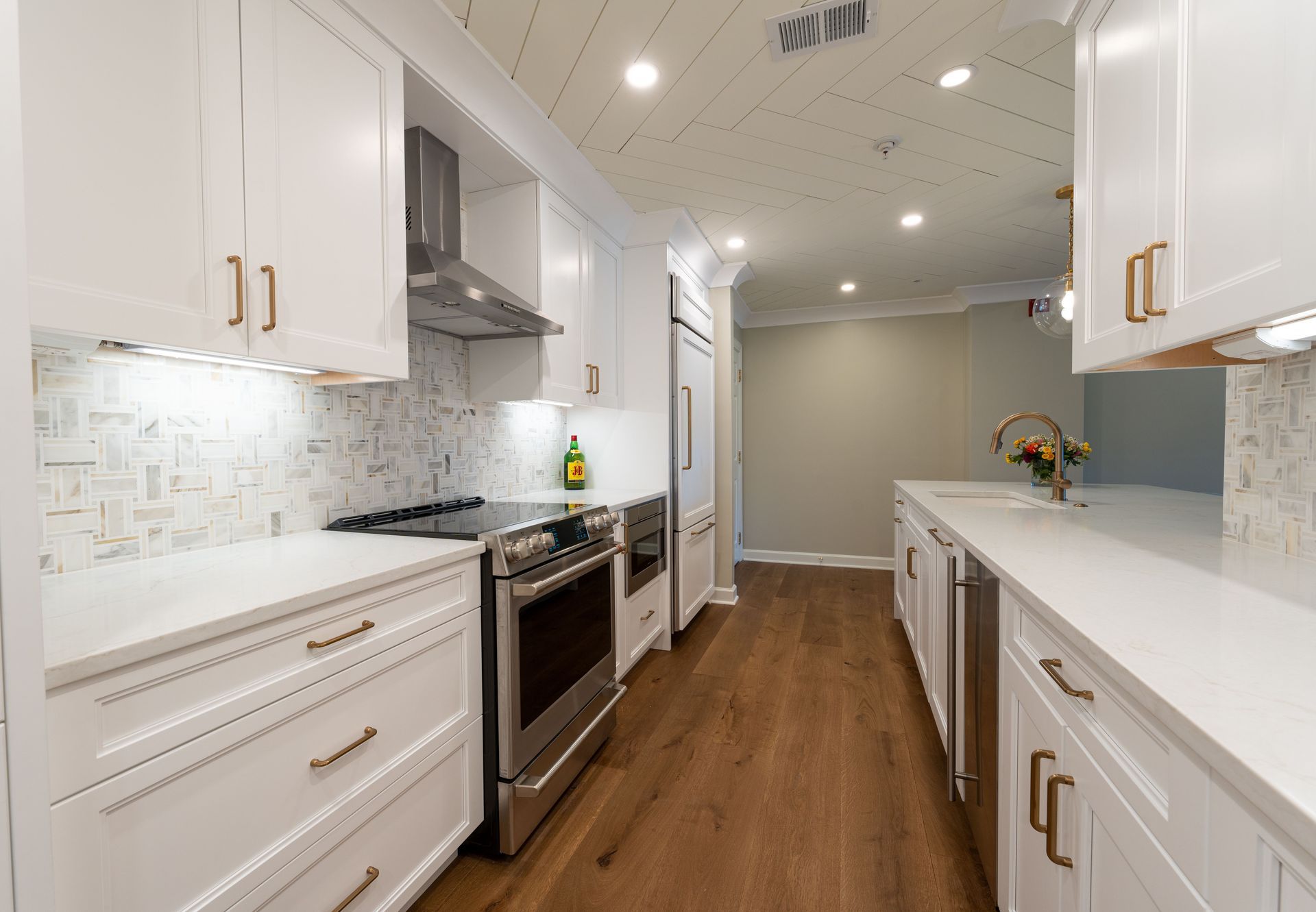 Bright white galley kitchen with stainless appliances, wood floor, and long white countertops.