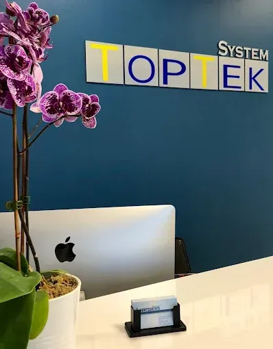 Toptek system office reception desk with laptop, plant, and purple flowers on a blue wall