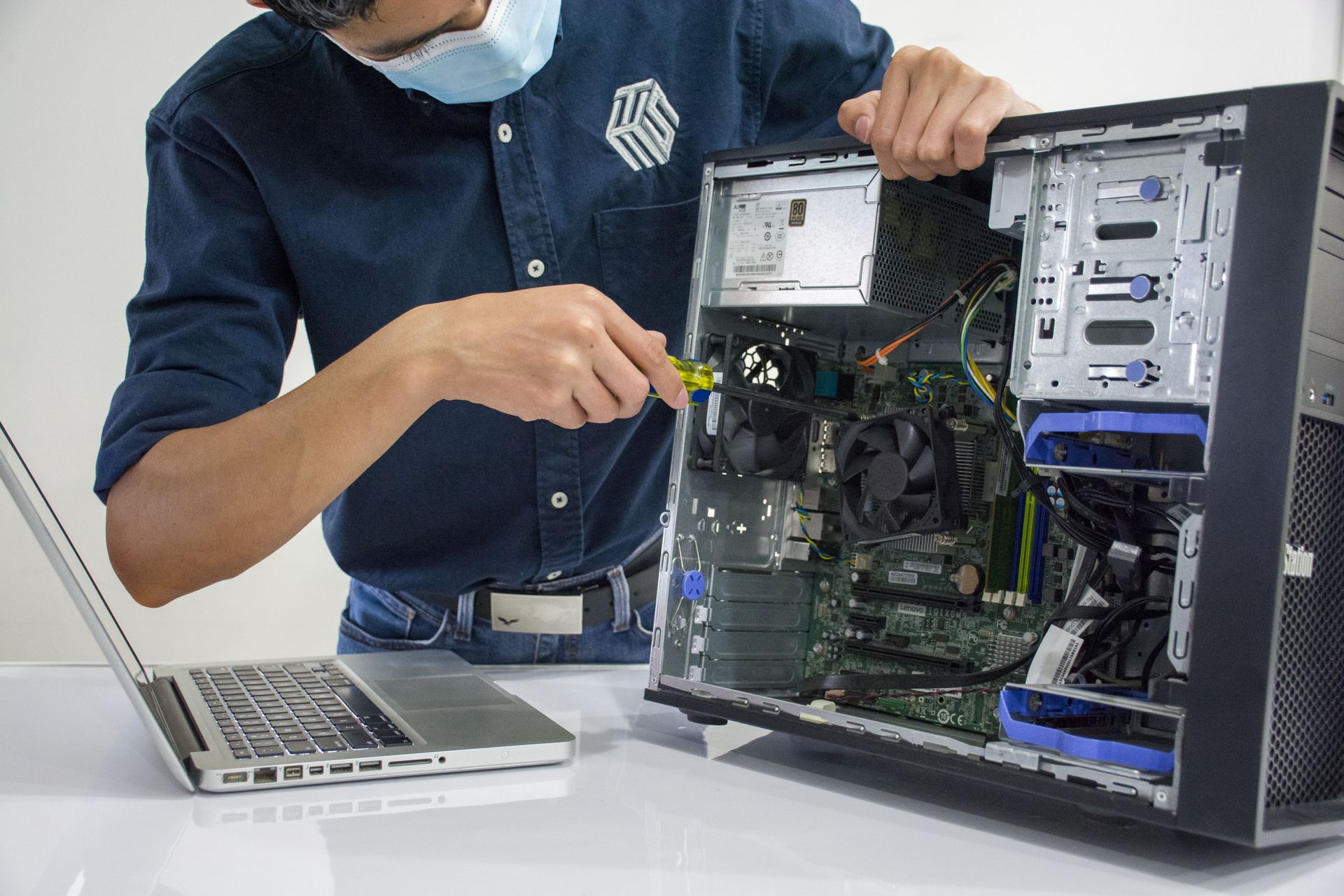 Technician working inside a desktop PC beside a laptop on a white desk