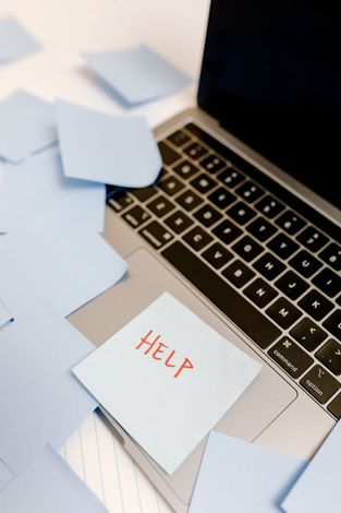 Sticky note reading “HELP” on a laptop keyboard, surrounded by scattered papers.