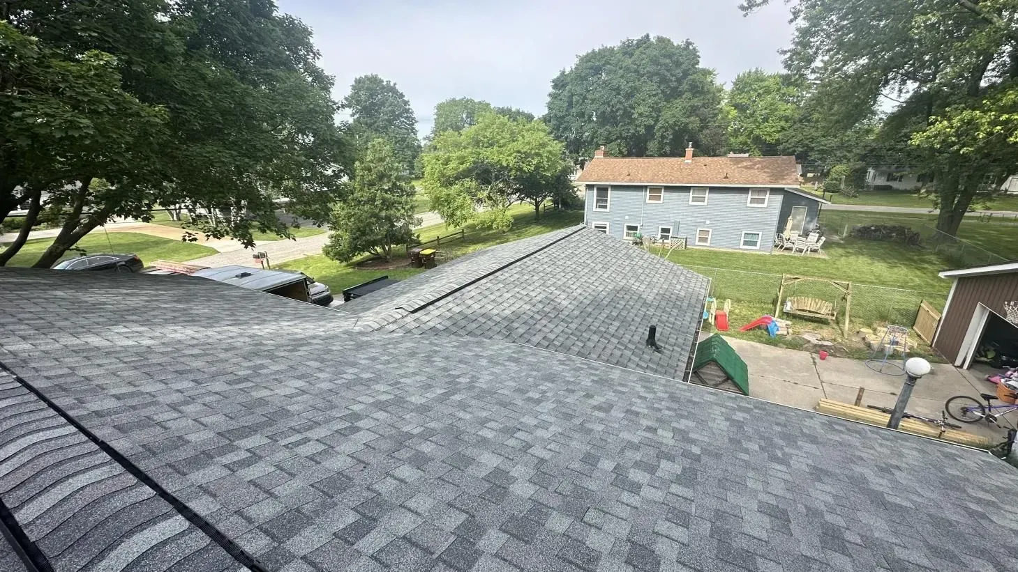 A roof with a lot of shingles on it and a house in the background.