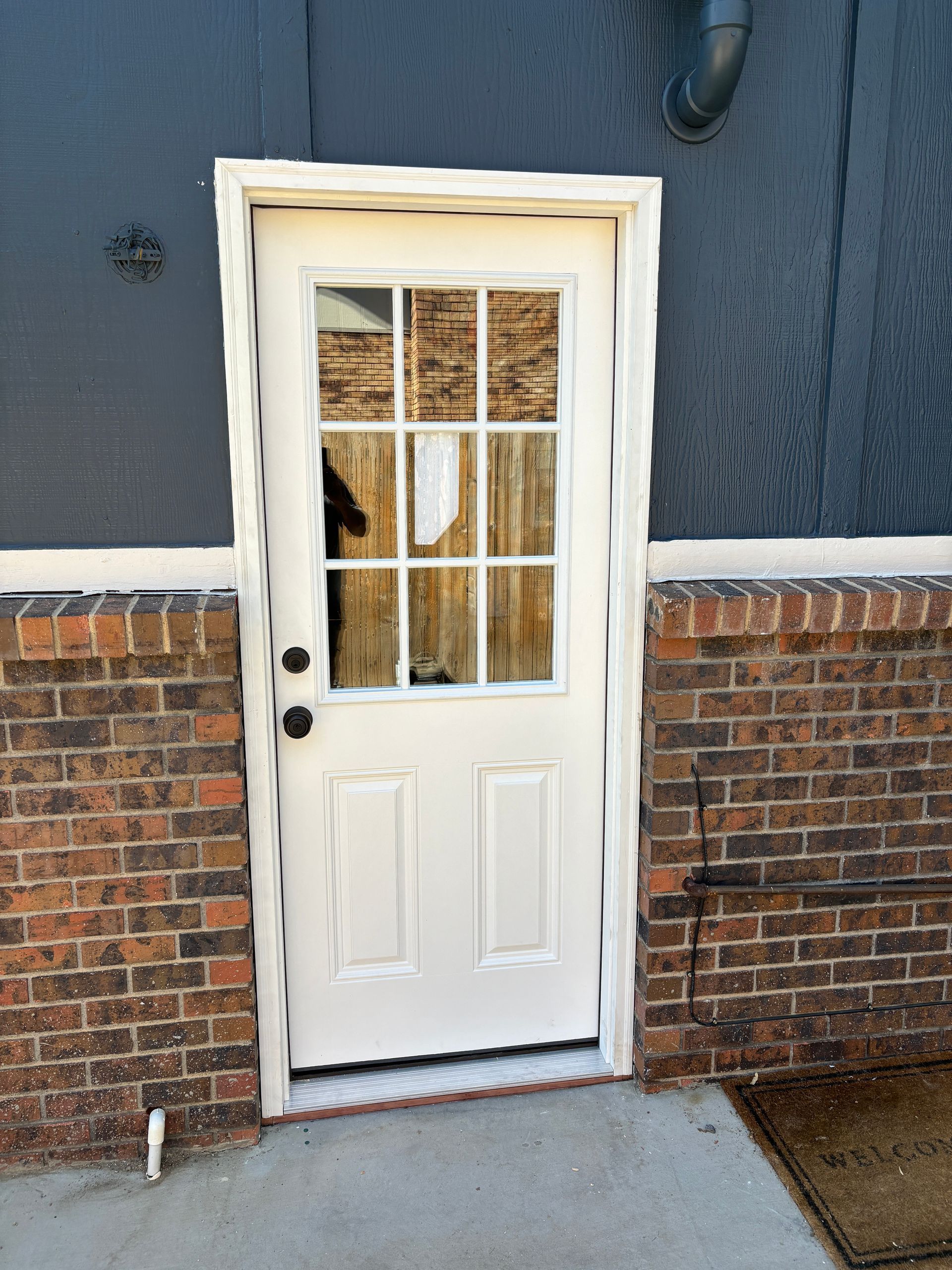 White exterior door with glass panes and sidelights, set in brick and dark siding.