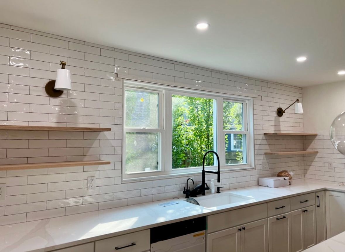 Kitchen with white tile backsplash, shelves, window over sink, and sconce lighting.