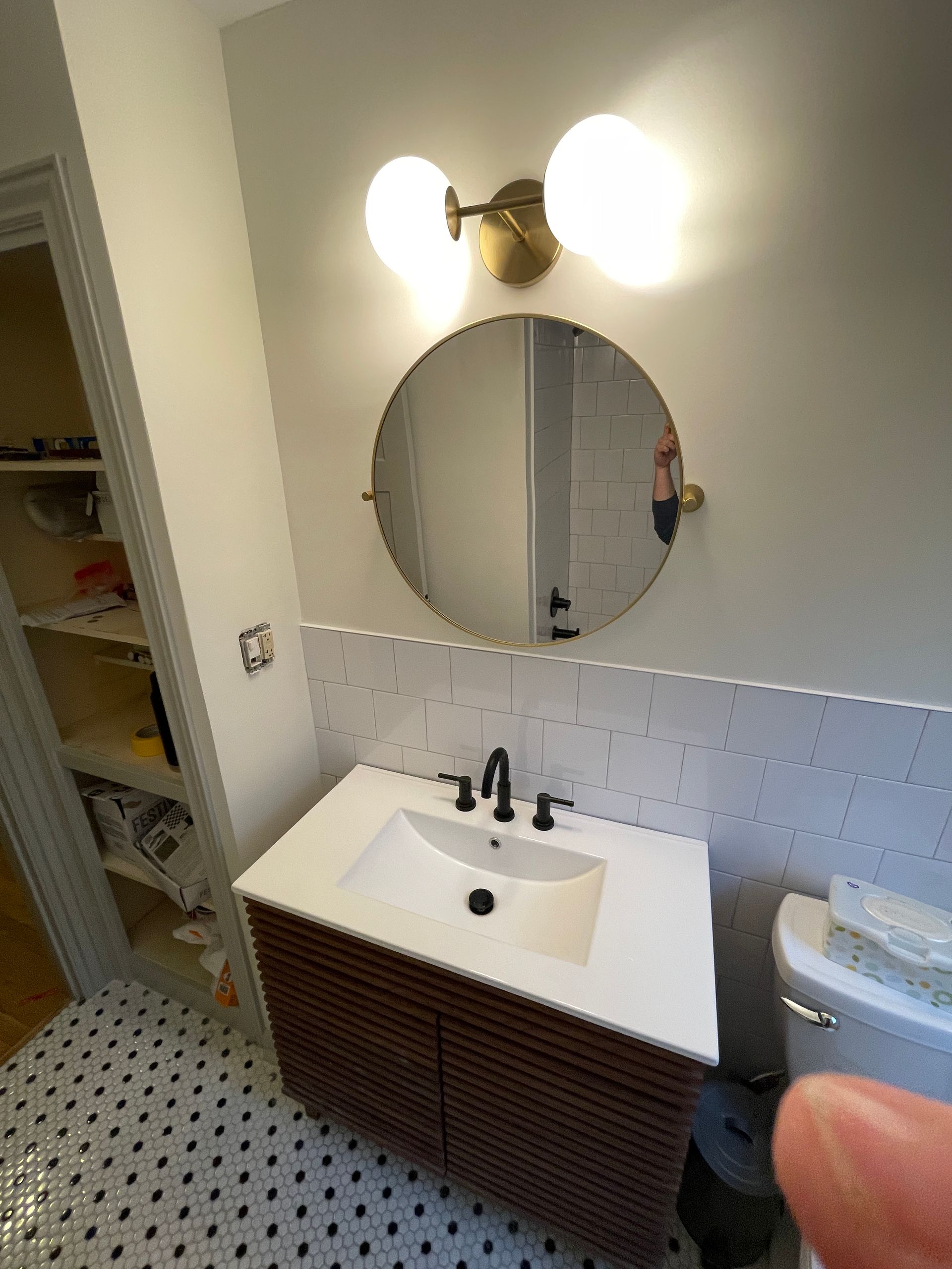 Bathroom with a round mirror, vanity, and globe light fixture. Black and white tile floor.