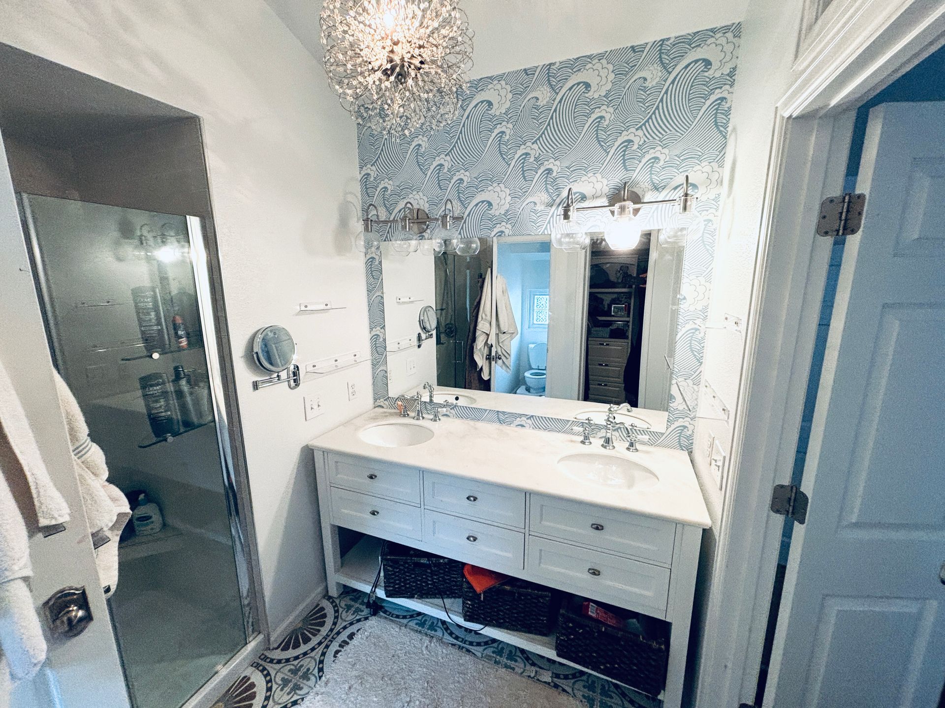 Bathroom with white vanity, double sinks, patterned wallpaper, and shower.