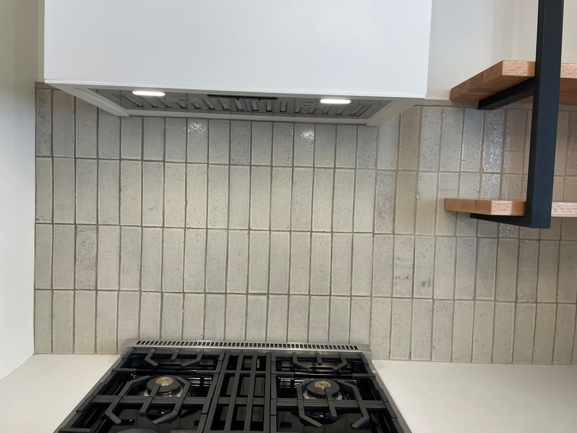 Kitchen backsplash with a white hood, gas stovetop, and two-tier wooden shelf.