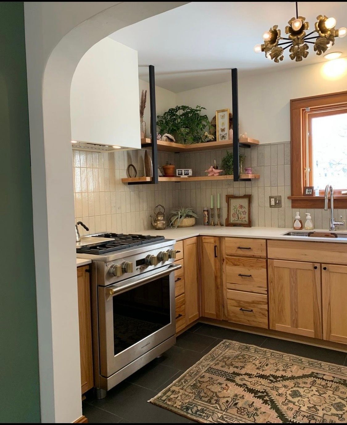 Kitchen with stainless steel range, light wood cabinets, open shelves, and rug.