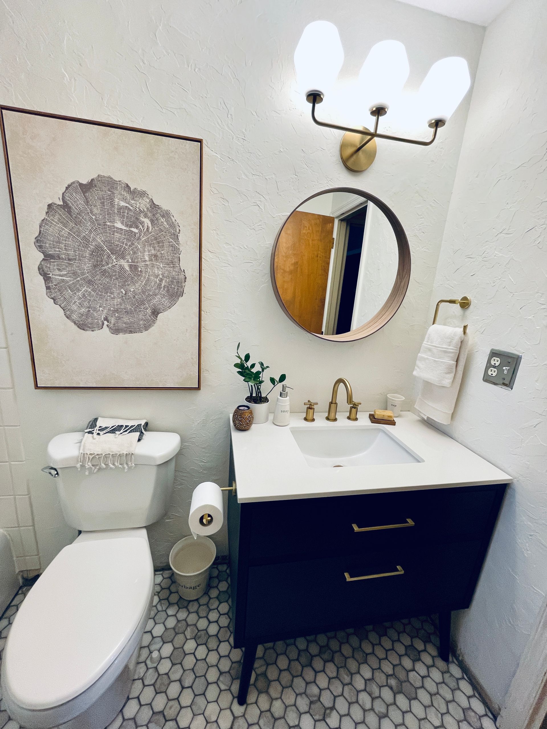 Bathroom with black vanity, round mirror, floral art, and mosaic floor.