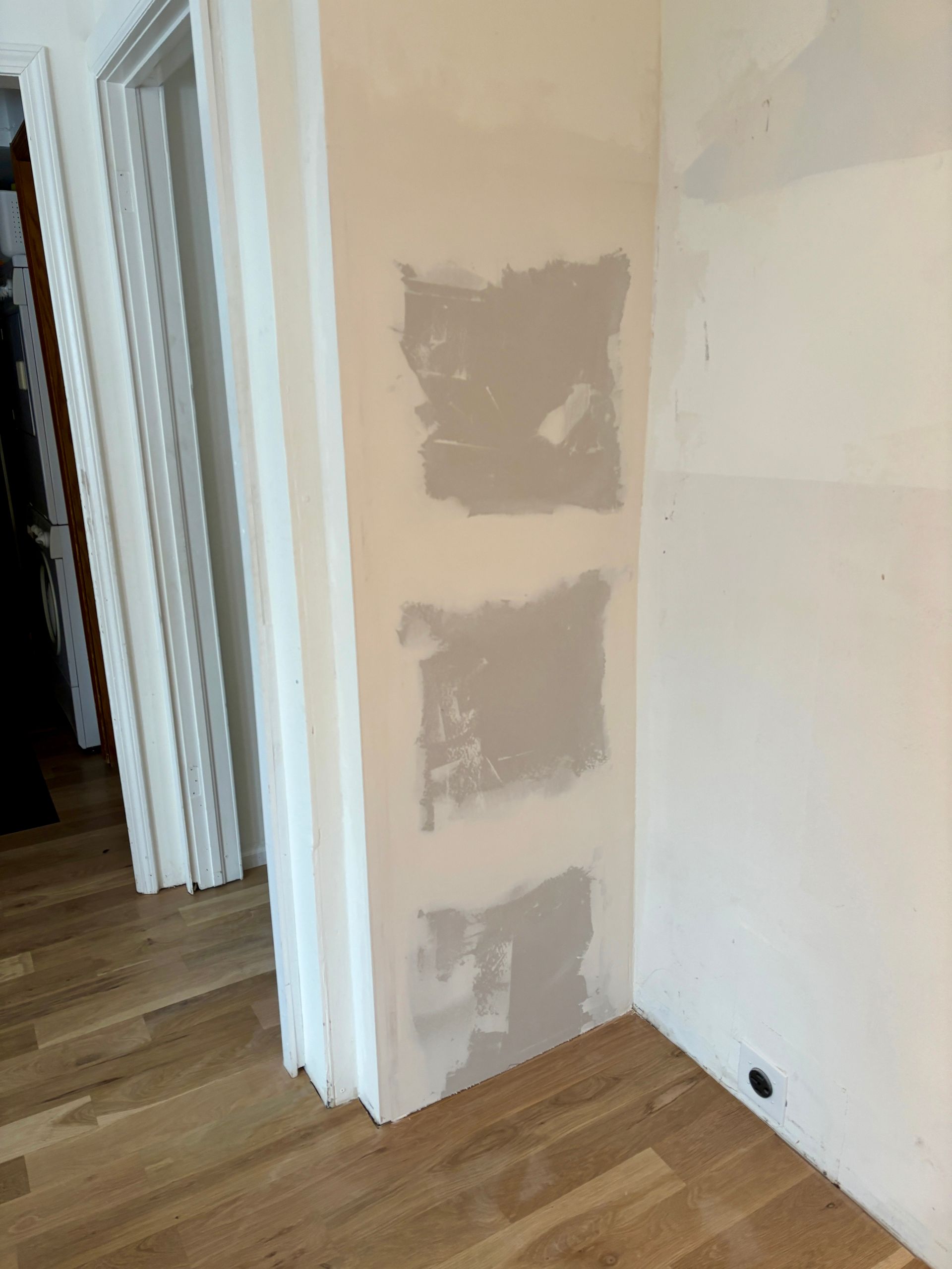 Three gray paint swatches on a beige wall in a room with a wooden floor.