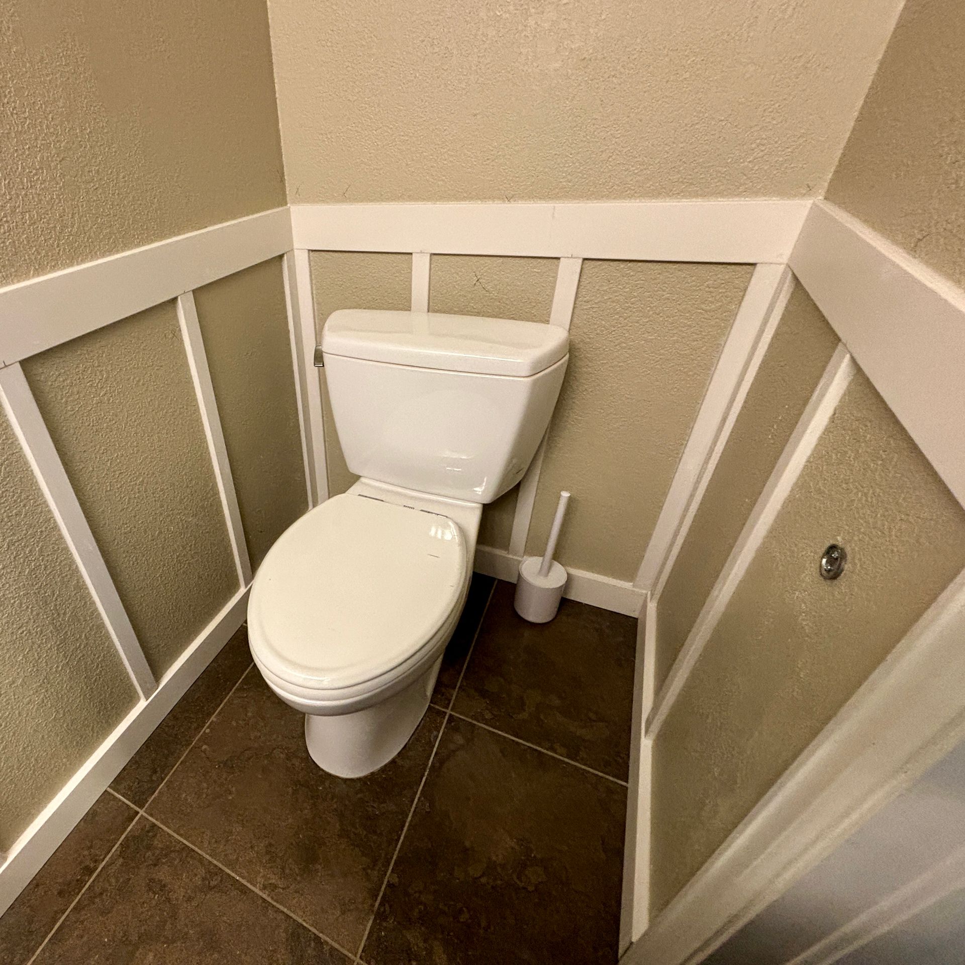 White toilet in a small bathroom with brown tile floor and textured tan walls with white trim.