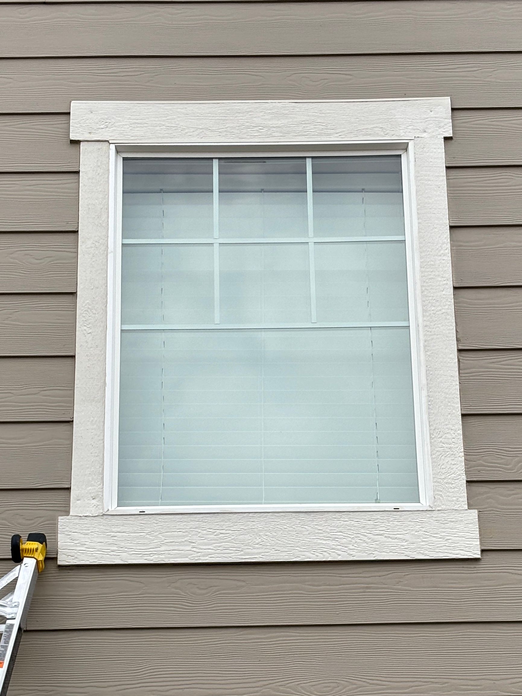 Window with white blinds, white trim, and stucco border on gray siding.