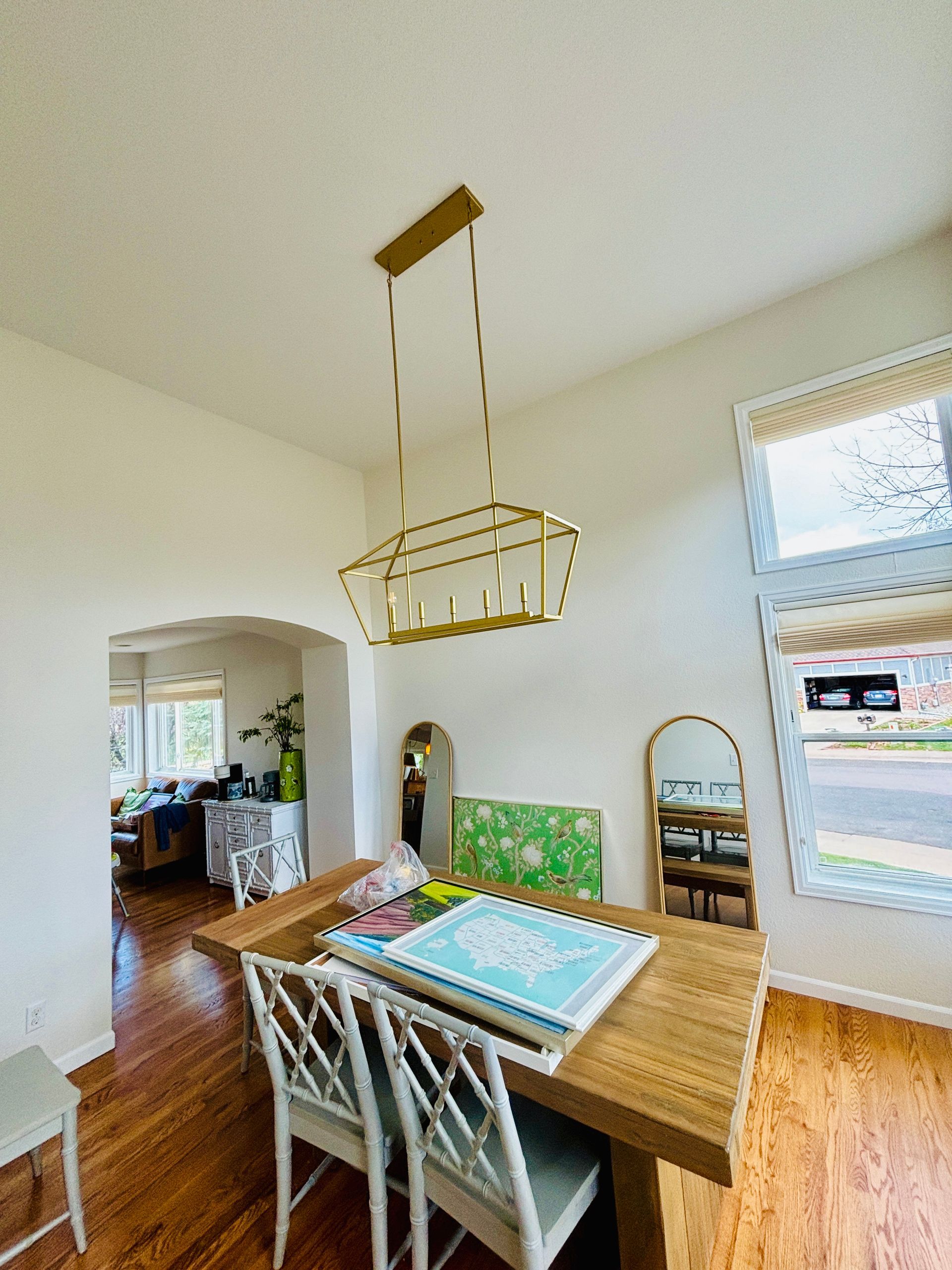 Dining room with light-colored walls, wooden table, and gold chandelier. Two chairs are pulled up to the table.