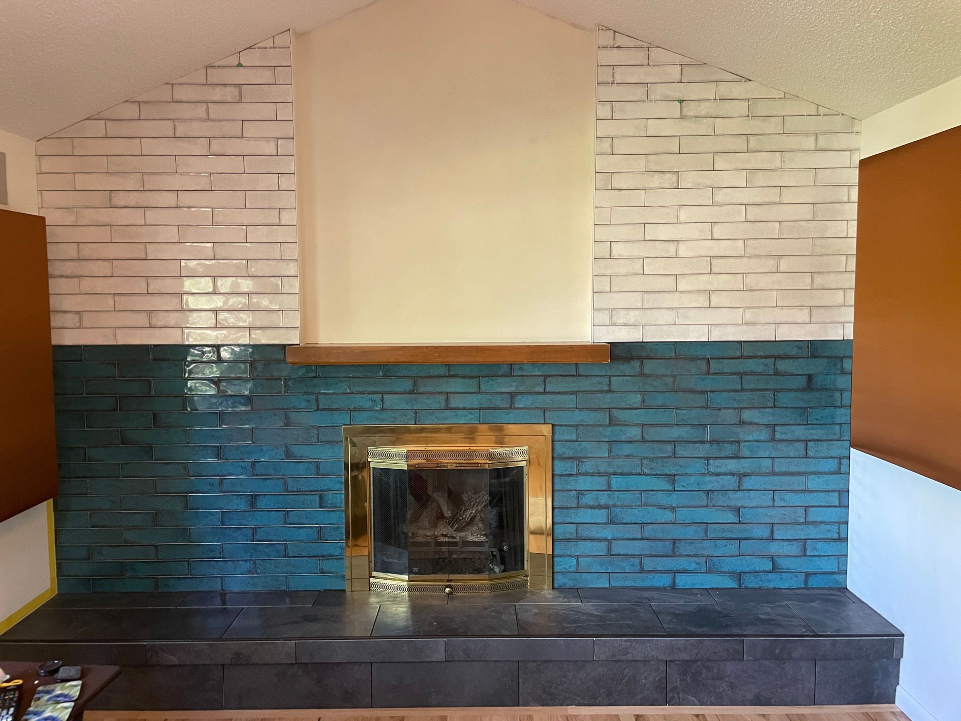 Fireplace with teal and white brick, gold fireplace surround, wood mantle, and dark hearth.