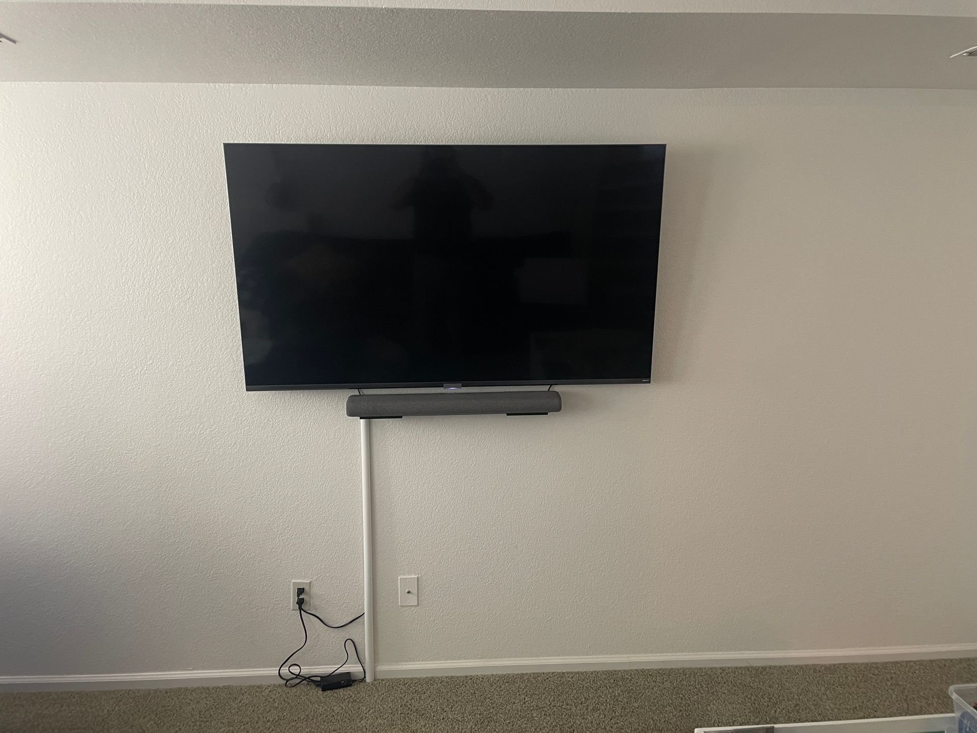 A flat-screen TV and soundbar mounted on a white textured wall with a cable running down to a power outlet.