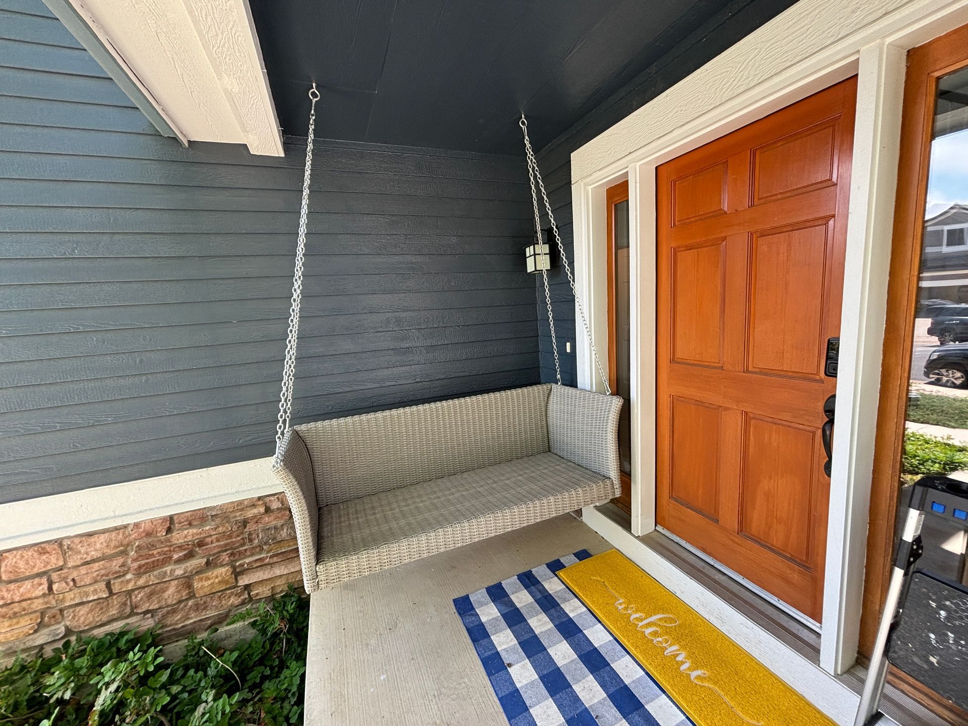 Front porch with a wicker swing, blue-gray siding, and a wooden door.