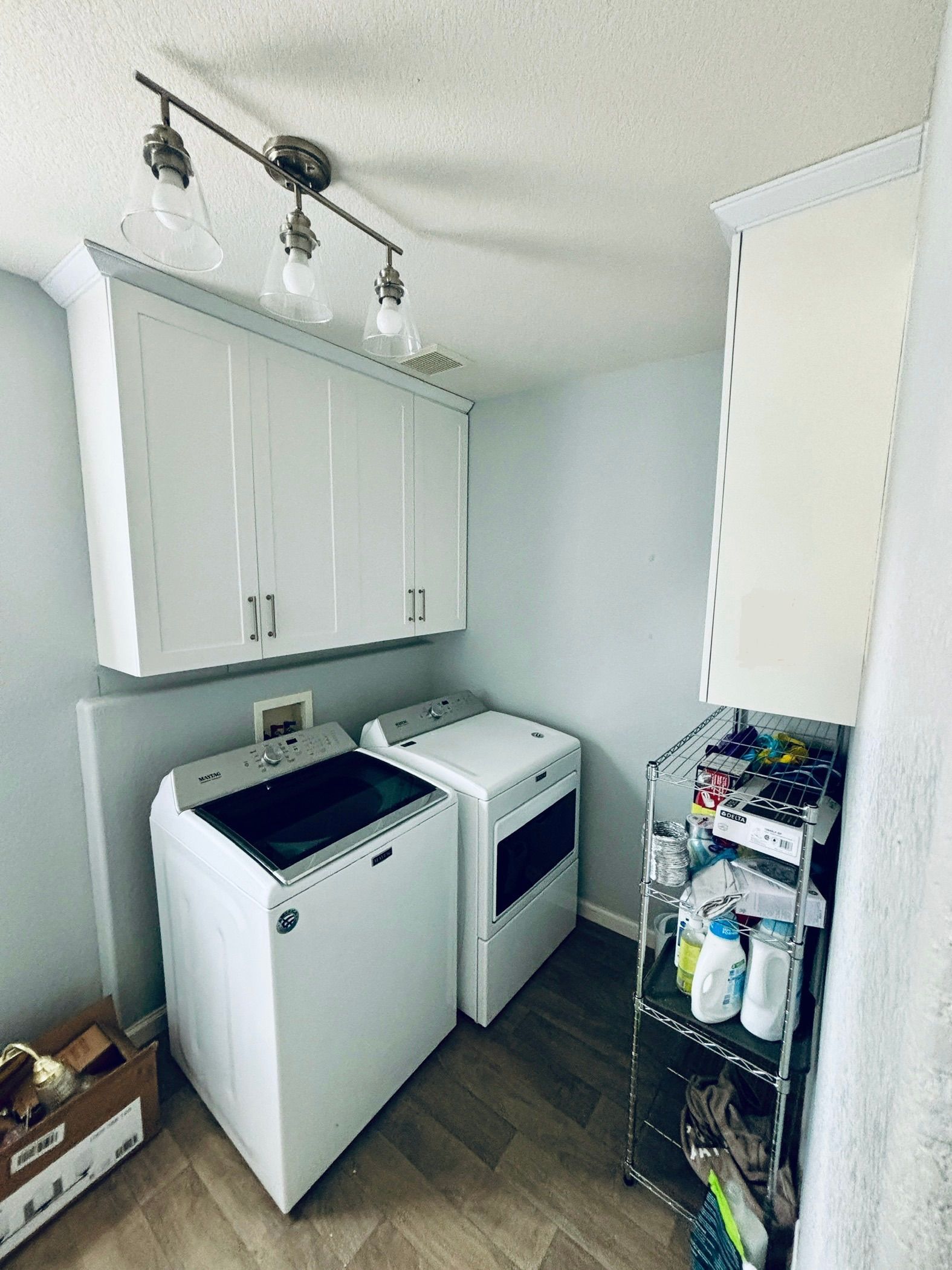 A laundry room with white appliances, overhead cabinets, and a shelving unit.