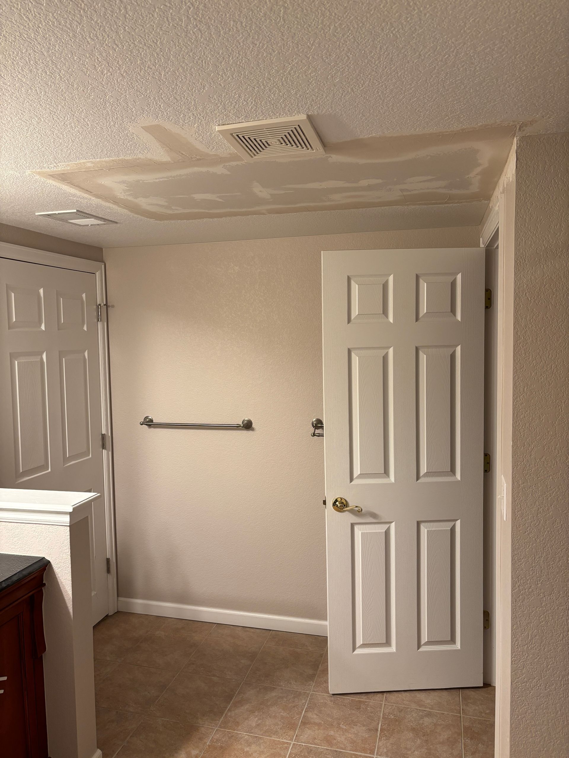 Bathroom with water damage on the ceiling, ajar door, towel rack, and textured walls and ceiling.