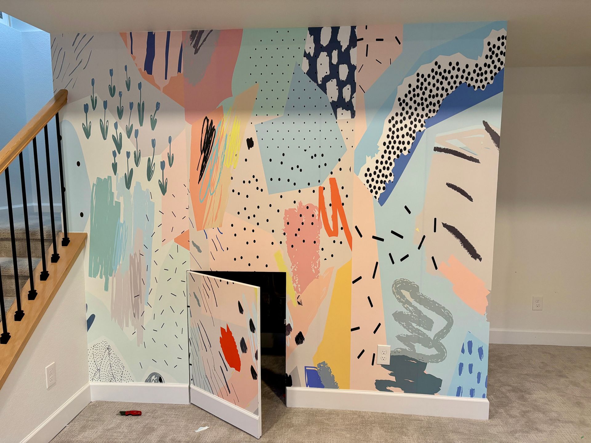 Colorful abstract mural with a hidden door under a staircase.
