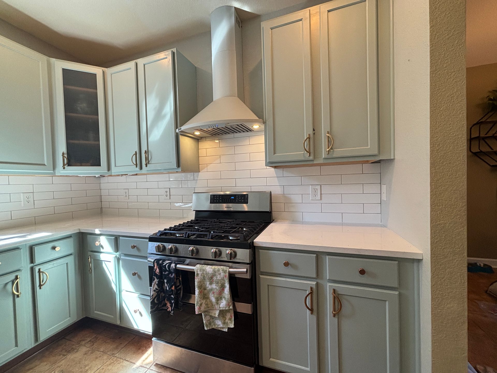 Kitchen with pale green cabinets, white backsplash and countertops, stainless steel stove, and range hood.